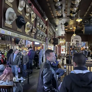 a crowd of people sitting at tables with hats hanging from the ceiling