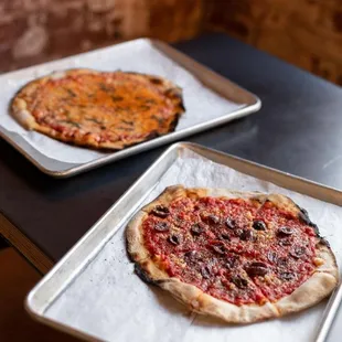 two pizzas on pans on a table