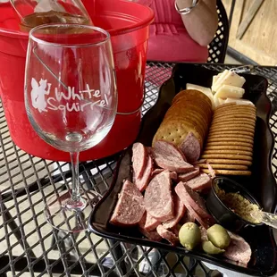 a glass of wine and a platter of meat and cheeses