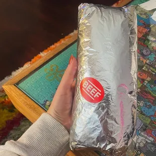 a person holding a sandwich wrapped in foil