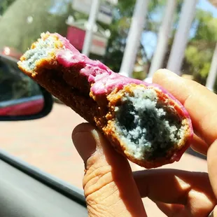 a hand holding a donut with pink icing