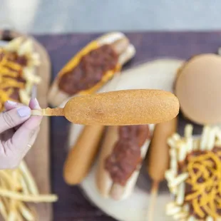 a person holding a hot dog with chili and cheese