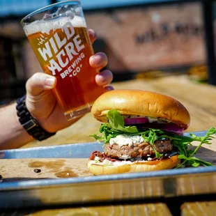 a hand holding a beer and a burger