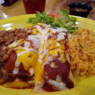 Two tamales covered in red chile, pinto beans, Spanish rice.