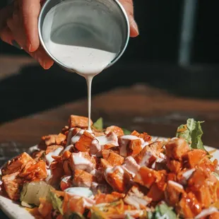 a person pouring dressing on a plate of food