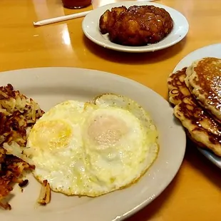 Eggs over medium, hashbrowns, pancakes and apple fritter.