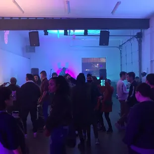 Back room of event space.  Stage in far back; L-shaped bar on right