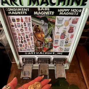 a hand holding a coin in front of an art machine