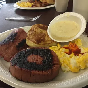 Breakfast with bologna, sausage, eggs, grits and pancake.