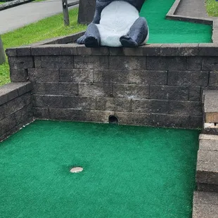 a giant panda bear sitting on the edge of a miniature golf course