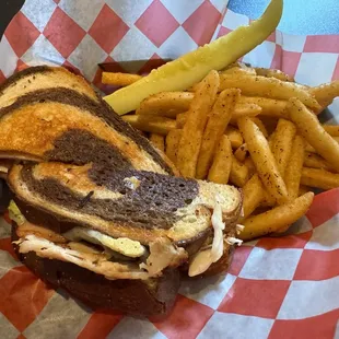 Rachel sandwich with pickle spear and seasoned fries.