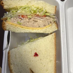 Tuna salad sandwich in white bread with lettuce, tomato, and cheddar cheese.