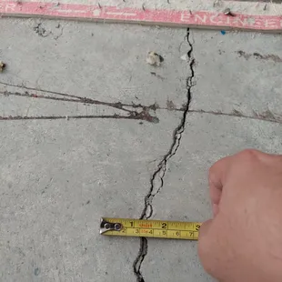 a person measuring a crack in concrete
