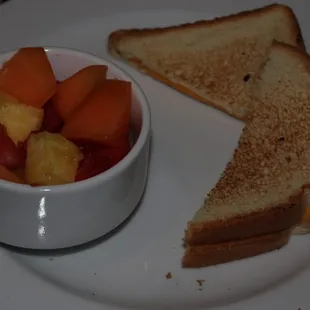 a white plate with a sandwich and a bowl of fruit