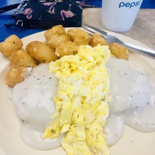 Gravy biscuit with scrambled eggs on top and a side of tots