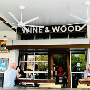 people sitting at tables in front of a wine and wood store