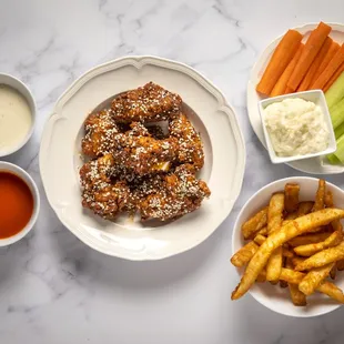 a plate of chicken wings, carrots, celery sticks, and dips