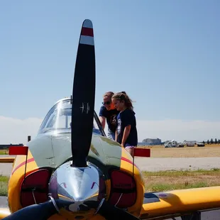 A Wings Over the Rockies summer camp student volunteer shows the inside of a cockpit to a student.