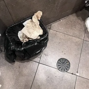 a trash bag on the floor next to a drain