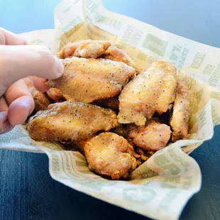 a hand holding a basket of chicken wings