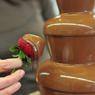 a strawberry being dipped into a chocolate fountain