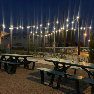 a row of picnic tables with lights strung over them