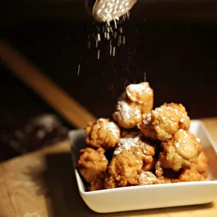 powdered sugar being sprinkled on a pile of fried food