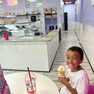 a boy sitting at a table with a cup of ice cream
