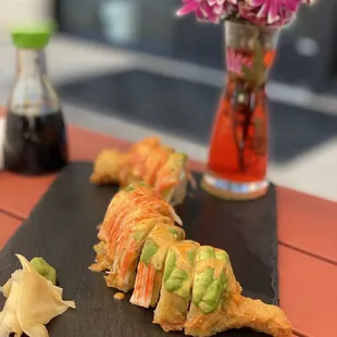 a sushi roll on a slate board with a vase of flowers in the background