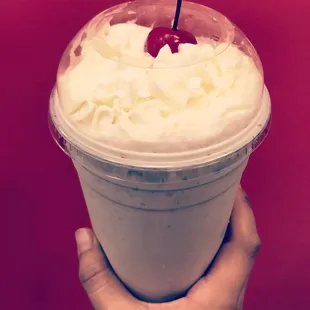 a hand holding a cup of ice cream with a cherry on top