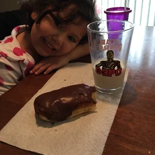 a little girl sitting at a table with a chocolate donut and a glass of milk