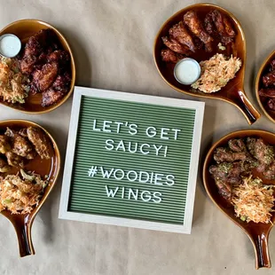 five bowls of food and a sign that says let&apos;s get saucy woodies wings