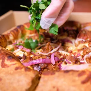 a hand sprinkling a piece of parsley on top of a pizza