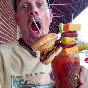 a man holding a bloody drink and a sandwich