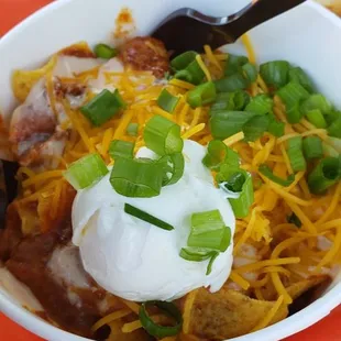 Totchos, tater tots covered with chili, cheddar cheese, sour cream, queso, tomatoes, corn chips, and green onions.