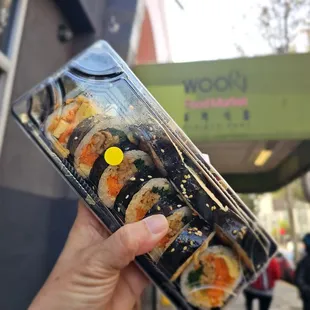a hand holding a box of sushi