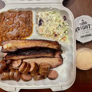 Texas Trinity = Smoked sausage, 2 pork ribs, 1 slice of brisket. Smoked beans and coleslaw sides. Original and Alabama white BBQ sauces.