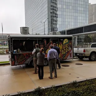 a group of people standing in front of a taco truck