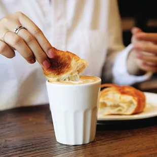 a person dipping a piece of bread into a cup of coffee