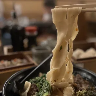 a closeup of the noodles being lifted by chopsticks