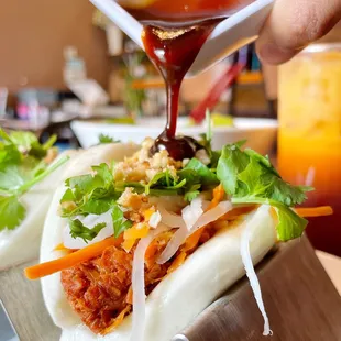 a person pouring sauce on a bun