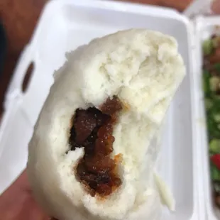 a hand holding a bun with meat and vegetables