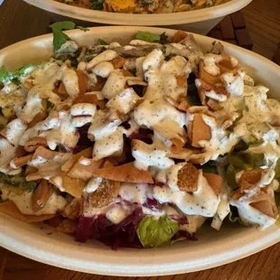 Salad bowl with vegetable toppings, pita strips, and white sauce.