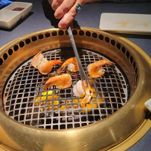a person using tongs to stir shrimp on a grill