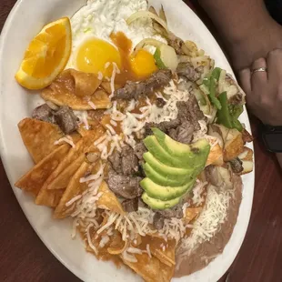 Chilaquiles and eggs with added carne asada and avocado