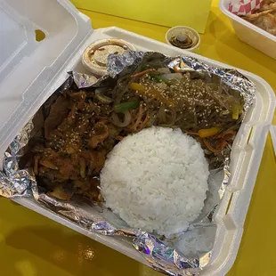 a takeout container with rice, meat, and vegetables