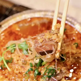 a person holding chopsticks over a bowl of soup