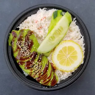 a bowl of food with rice, cucumbers, avocado, and sliced cucumbers