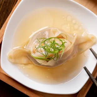 a dumpling in a bowl of soup with chopsticks