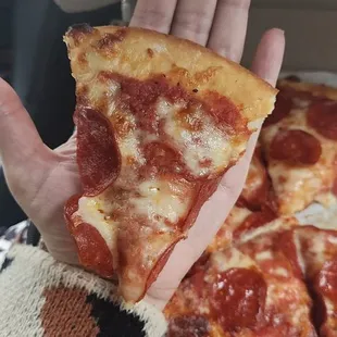 a hand holding a slice of pepperoni pizza